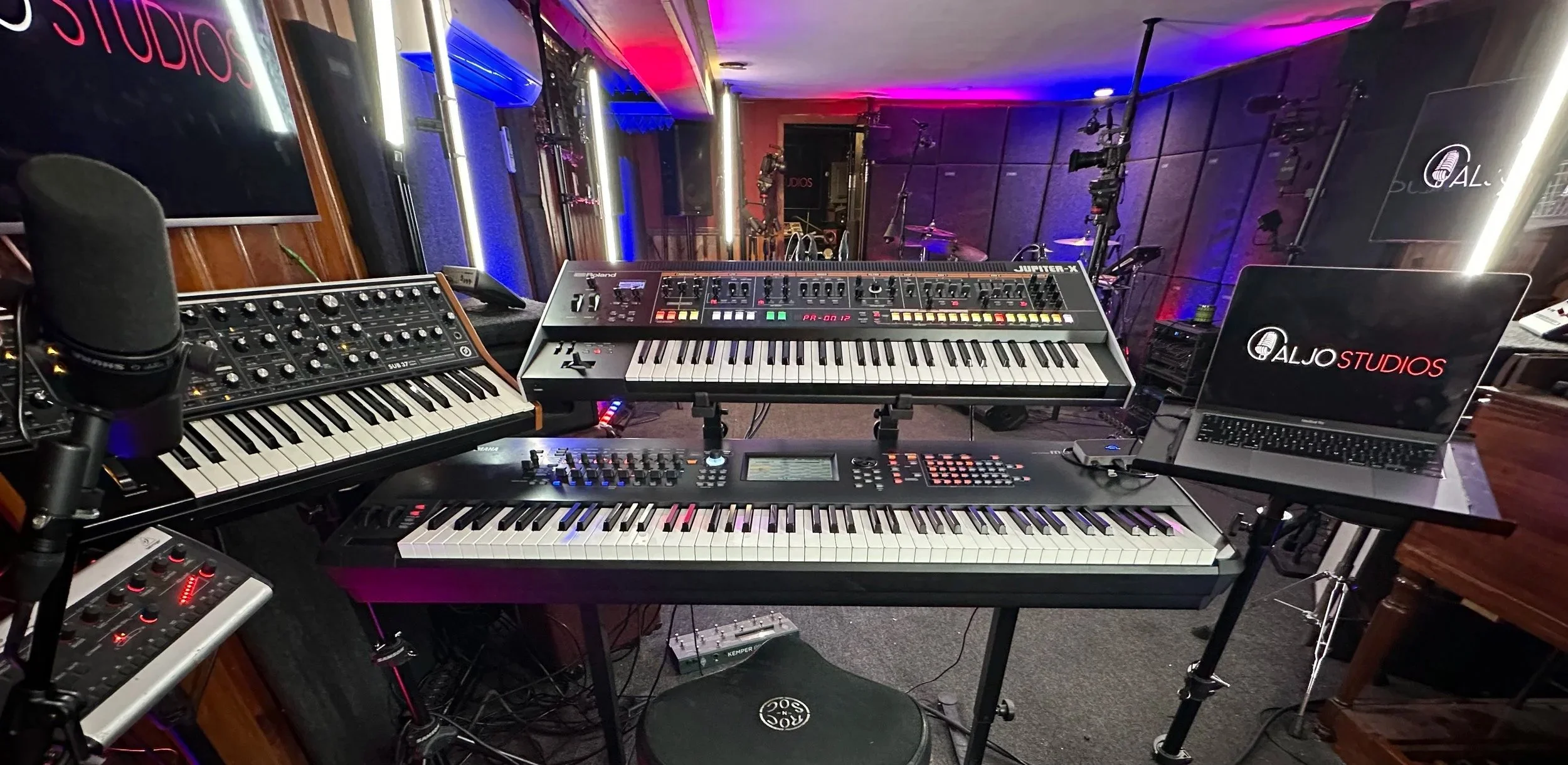 ALJO Studios filled with keyboards, production equipment, and blue-purple studio lighting